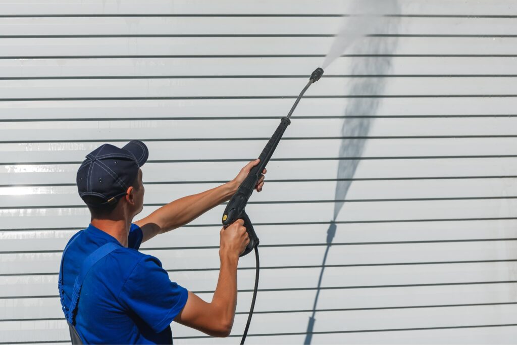worker-overalls-washes-white-wall-from-siding-with-water-gun-min
